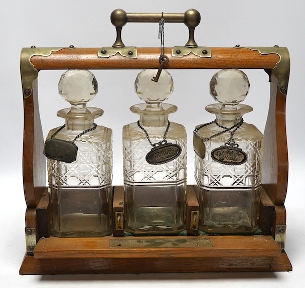 A Victorian oak three decanter tantalus with four spirit labels, and key, 37cm wide. Condition -fair